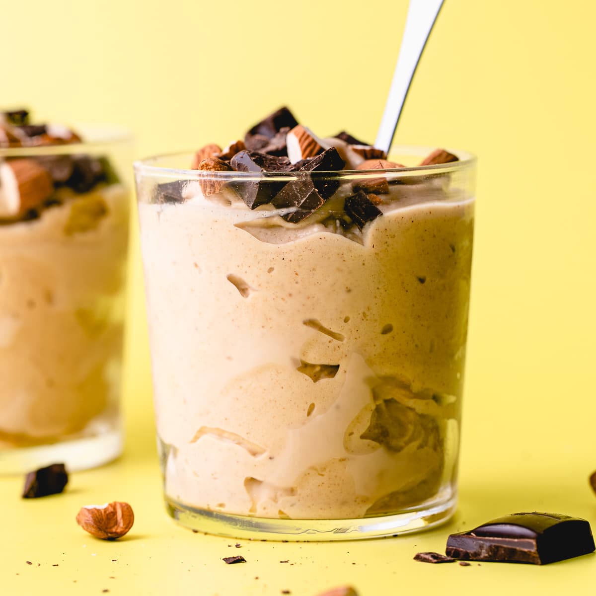 head on view of vegan chunky monkey ice cream in glass cup with spoon and items surrounding.