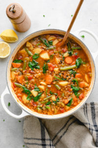 top down view of pot with fresh cooked vegan lentil soup with items surrounding.