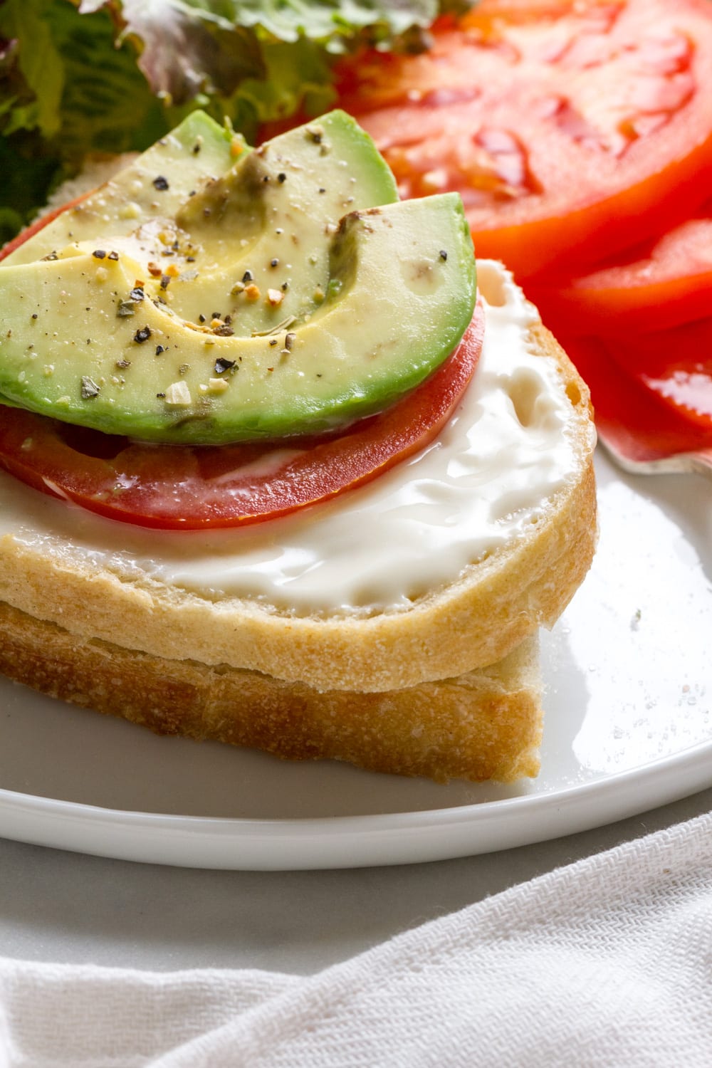 side shot of a slice of artisan bread topped with fresh vegan mayo, sliced tomato and avocado