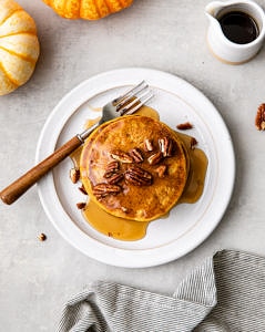 top down view of vegan pumpkin pancakes with pure maple syrup on a plate.