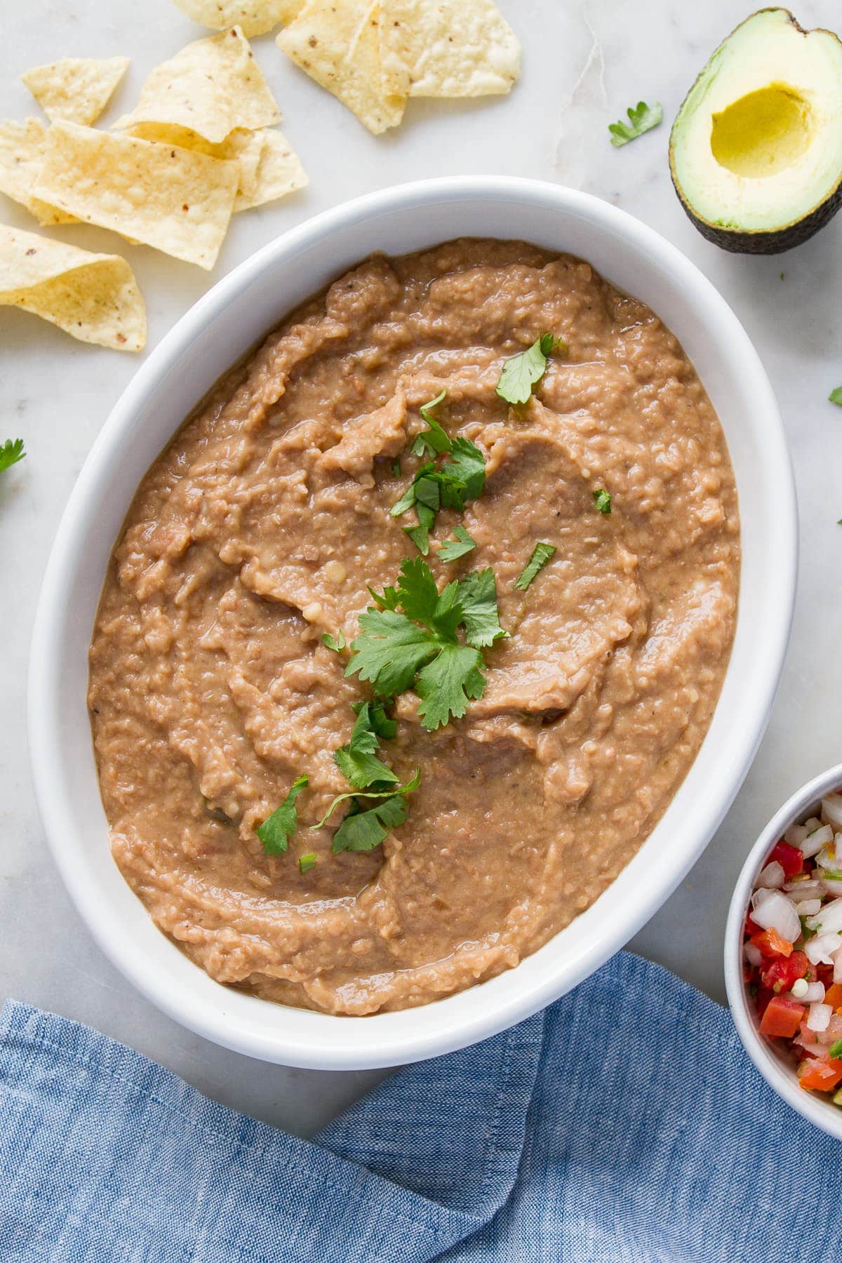 top down view of refried beans in a white serving bowl with chopped cilantro sprinkled overtop.